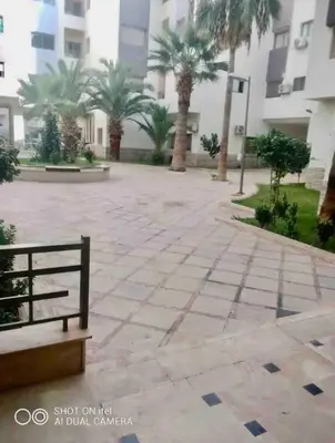a bench in a courtyard with palm trees and a building at Appartement la Cañada in Ville Nouvelle