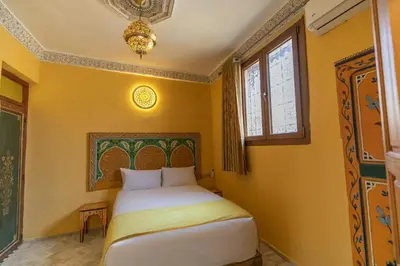 a bedroom with a bed with yellow walls and a chandelier at Dar Golden Ziat in Fès