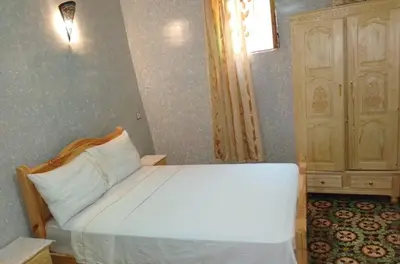 a bedroom with a white bed and a wooden cabinet at Appartement lala Houriya fez in Fès