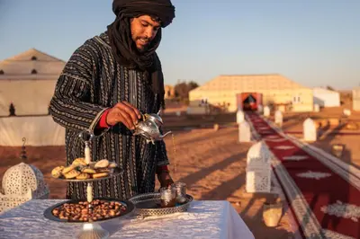 a man standing next to a table with a plate of food at Luxury Camp Glamping in Merzouga