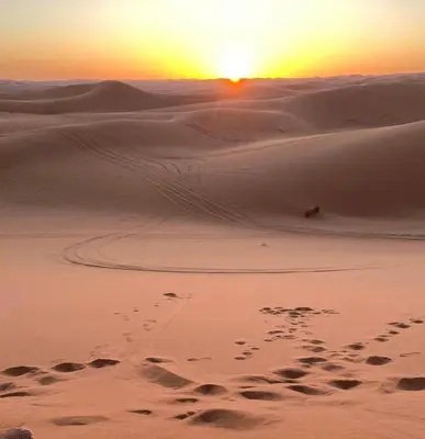 a sunset in the desert with footprints in the sand at Desert Mhamid Luxury Camp in Mhamid El Ghizlane