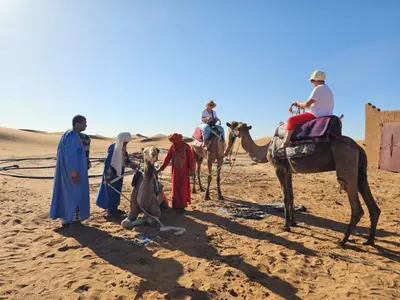 a group of people on camels in the desert at Desert Mhamid Luxury Camp in Mhamid El Ghizlane