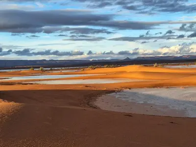 a desert with sand and water and a cloudy sky at Desert Mhamid Luxury Camp in Mhamid El Ghizlane
