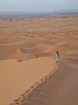 a man walking down a sand dune in the desert at Desert Mhamid Luxury Camp in Mhamid El Ghizlane
