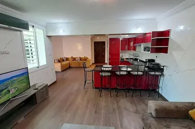 a kitchen and living room with red cabinets and a table at Appartement Jasmine Atlas Center in Fès