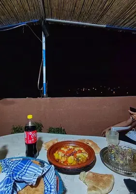 a table with a pizza and a bottle of soda at Hostel Ighounane in Ouarzazate