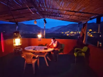 a man sitting at a table on a balcony at night at Hostel Ighounane in Ouarzazate
