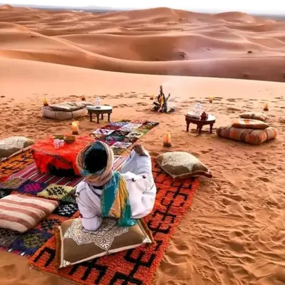 a woman sitting on a blanket in the desert at Merzouga Dunes Luxury Glamping Camp in Merzouga