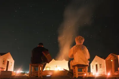 two people sitting on chairs watching a fire at night at The dune camp in Mhamid