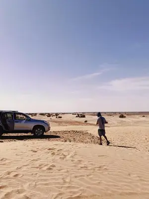 a man walking in the sand next to a car at Erg Chegaga Charming Camp in El Gouera