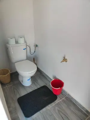 a bathroom with a toilet and a red bucket at Erg Chegaga Charming Camp in El Gouera