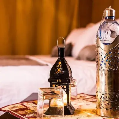 a table with a bottle and glasses and a bed at Cleopatra luxury camp in Merzouga