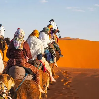 a group of people riding on camels in the desert at Cleopatra luxury camp in Merzouga