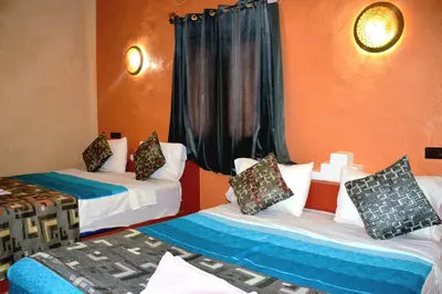 two beds in a room with orange walls at Kasbah Du Berger & Piscine in Merzouga