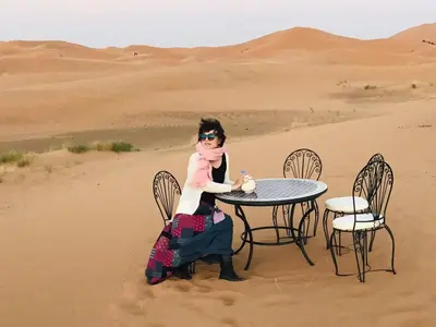 a woman sitting at a table in the desert at Merzouga Activities Camp in Merzouga
