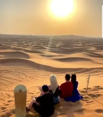 a group of people sitting on the beach watching the sunset at Merzouga Activities Camp in Merzouga