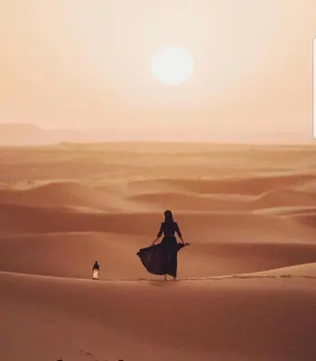 a woman walking through the sand in the desert at Merzouga Activities Camp in Merzouga