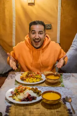 a man sitting at a table with plates of food at Merzouga Luxury Camp & Activities in Merzouga