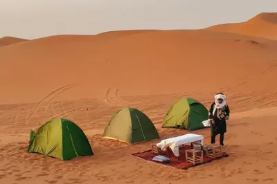 a man standing next to two tents in the desert at Canadien camp merzouga in Merzouga
