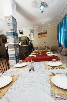 a group of tables in a restaurant with people in the background at Hotel De La Vallée in Aït Baha
