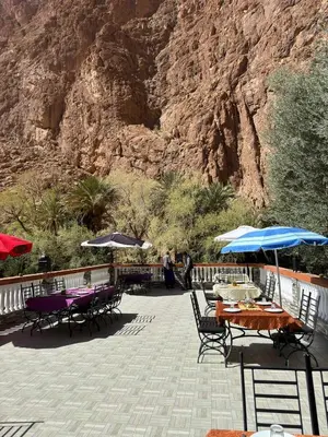 a group of tables and chairs with umbrellas in front of a mountain at Hotel De La Vallée in Aït Baha