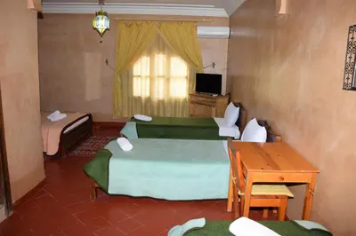 a room with two beds and a desk and a television at Kasbat Dar diafa Tourbist in Kalaat MGouna