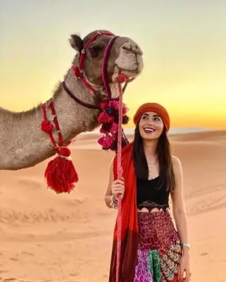 a woman standing next to a camel in the desert at Merzouga Sardegna Luxury Camp in Merzouga