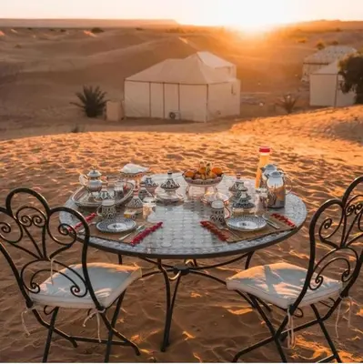 a table in the middle of the desert with chairs at Merzouga Sardegna Luxury Camp in Merzouga