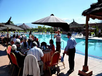 a group of people sitting at a table by a pool at Hôtel Jnane Ain Asserdoune in Oulad Yaïch