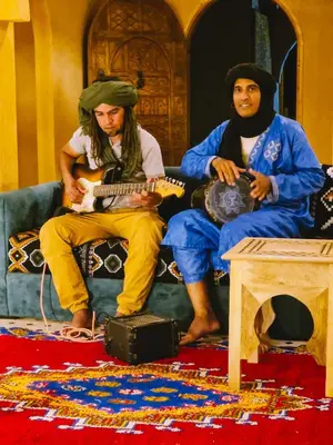 two men sitting on a couch playing guitars at Hotel Kasbah Riad Amnir in Mhamid