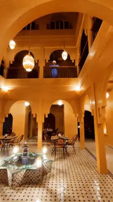 a man standing in a large room with tables and chairs at Hotel Kasbah Riad Amnir in Mhamid