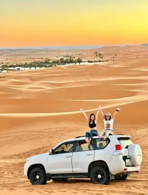 two people sitting on the roof of a car in the desert at Merzouga Sara Luxury Camp in Merzouga
