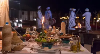 a table with food on it with people in the background at Merzouga Sara Luxury Camp in Merzouga