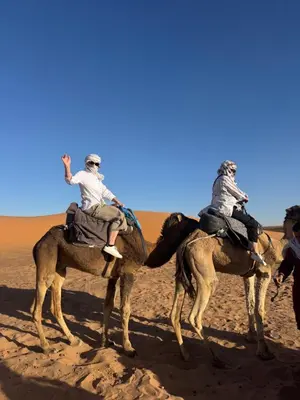 two people riding on the backs of camels in the desert at Ksar Merzouga in Merzouga