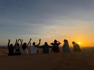 a group of people sitting in the desert watching the sunset at Ksar Merzouga in Merzouga