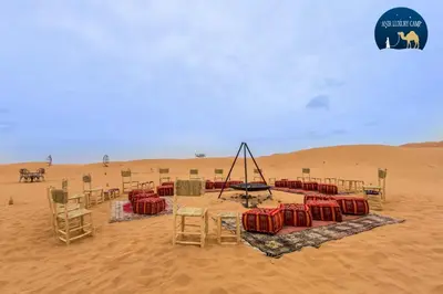 a desert with a table and chairs in the sand at Une Nuit de Rêve dans une Tente de Luxe - Expérience en plein désert ! in Merzouga