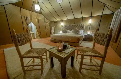 a bedroom with a bed and two chairs and a table at Une Nuit de Rêve dans une Tente de Luxe - Expérience en plein désert ! in Merzouga