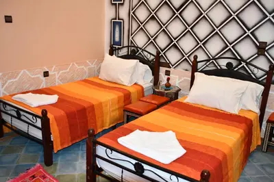 a room with two beds with orange and orange sheets at Hôtel La Vallée Des Oiseaux in Boumalne
