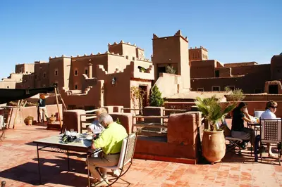 a group of people sitting at tables on a patio with buildings at Dar Kamar in Ouarzazate