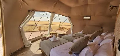 three beds in a room with a view of the desert at Royal Sahara Dome Camp in Merzouga