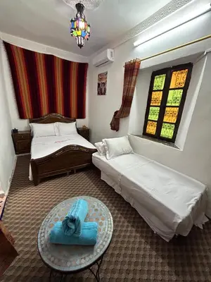 a bedroom with two beds and a table and a window at DarMouniaFès in Fès
