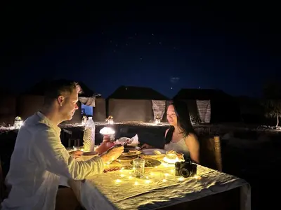 a man and a woman sitting at a table at night at Eco Merzouga luxury camp in Merzouga