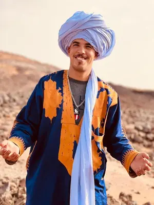 a man wearing a turban and smiling at the camera at Eco Merzouga luxury camp in Merzouga