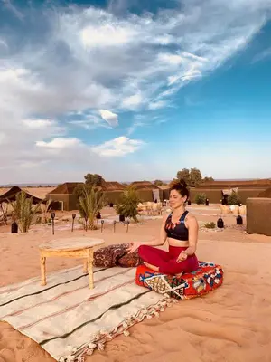 a woman sitting on a surfboard in the desert at Eco Merzouga luxury camp in Merzouga