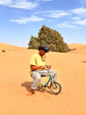a man sitting on a bike in the desert at Eco Merzouga luxury camp in Merzouga