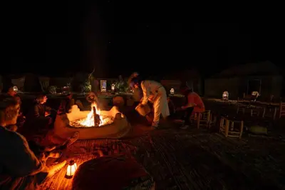 a group of people sitting around a fire pit at night at Eco Merzouga luxury camp in Merzouga