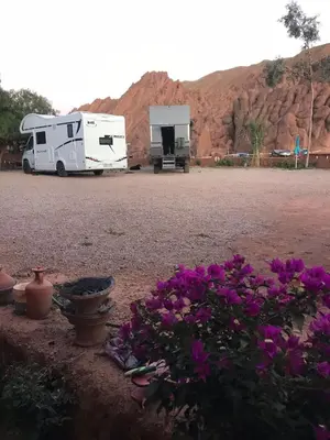 an rv parked in a parking lot with purple flowers at Camping Restaurant Pattes des singes in Aït Ougliff