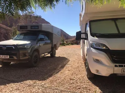a truck parked next to a camper on a dirt road at Camping Restaurant Pattes des singes in Aït Ougliff