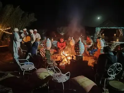 a group of people sitting around a fire at night at Luxury Desert Camp Erg Chegaga in El Gouera