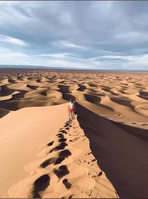 a person walking on a sand dune in the desert at Luxury Desert Camp Erg Chegaga in El Gouera